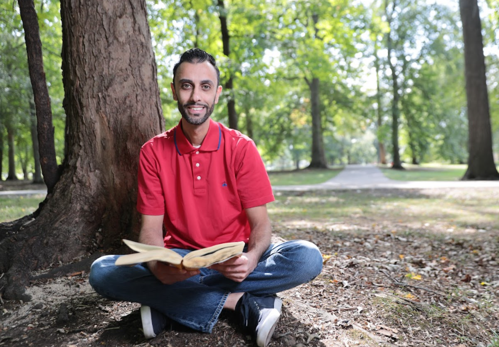 Man in red shirt sitting cross-legged outside, reading