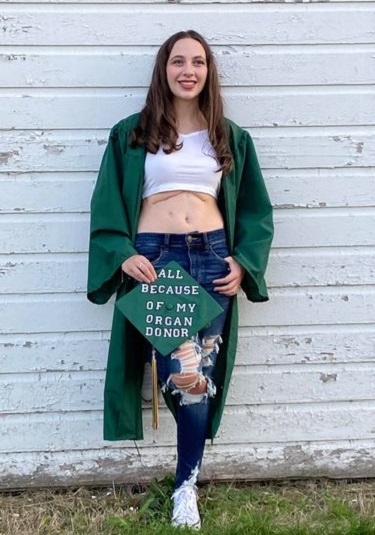 Young woman in cap and gown, cap says "All because of my organ donor" on top