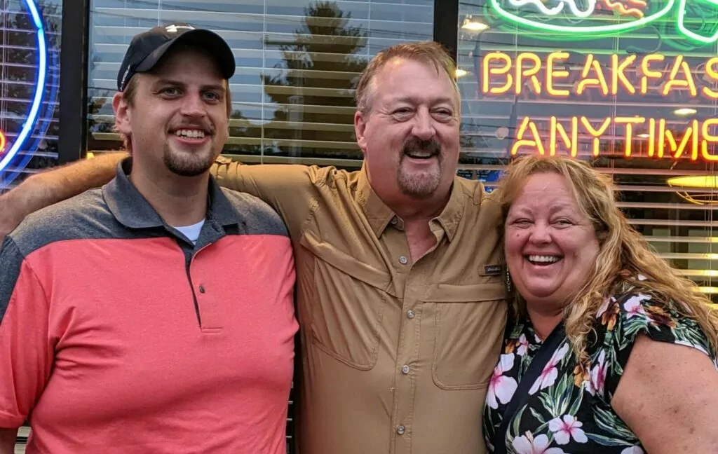 Two men and a woman with their arms around each other in front of a diner