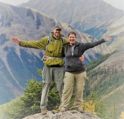 Man and woman with arms raised and mountains in the background
