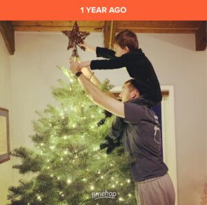 Man with child on his shoulders putting star on top of Christmas tree