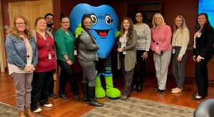 Hartley, chief mascot and giant blue heart, surrounded by a variety of people at new hire orientation