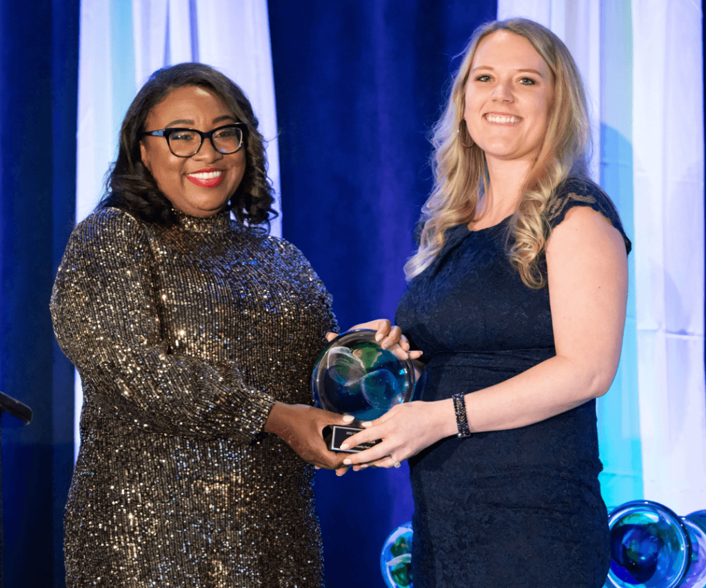 Woman presenting a blue and green glass award to another woman