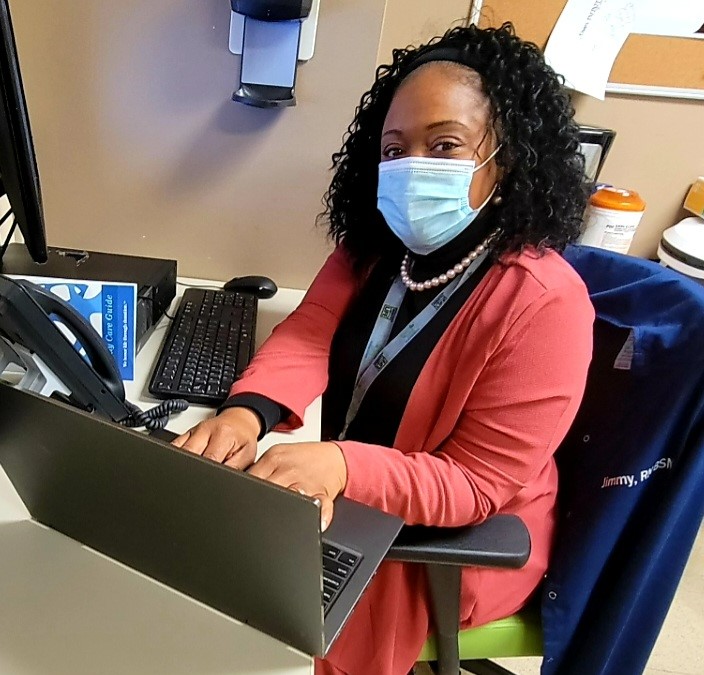 woman seated at desk, working on computer while wearing a surgical mask