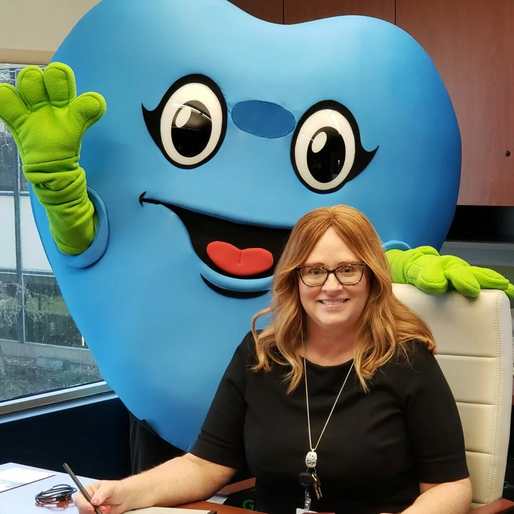 Woman seated at desk with blue heart mascot standing behind her