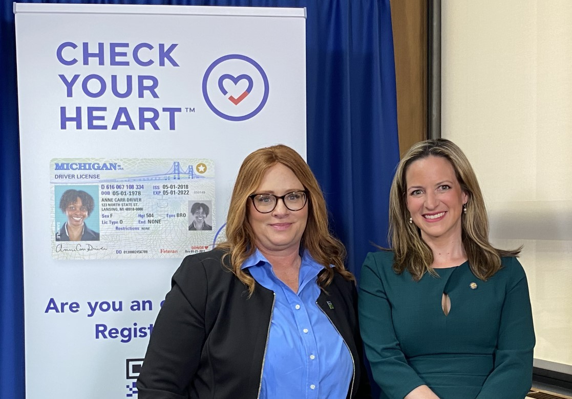 Two well-dressed women stand in front of "Check Your Heart" banner