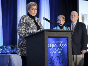 Woman at podium for Gift of Life Champions Gala, older couple looking on from beside the podium