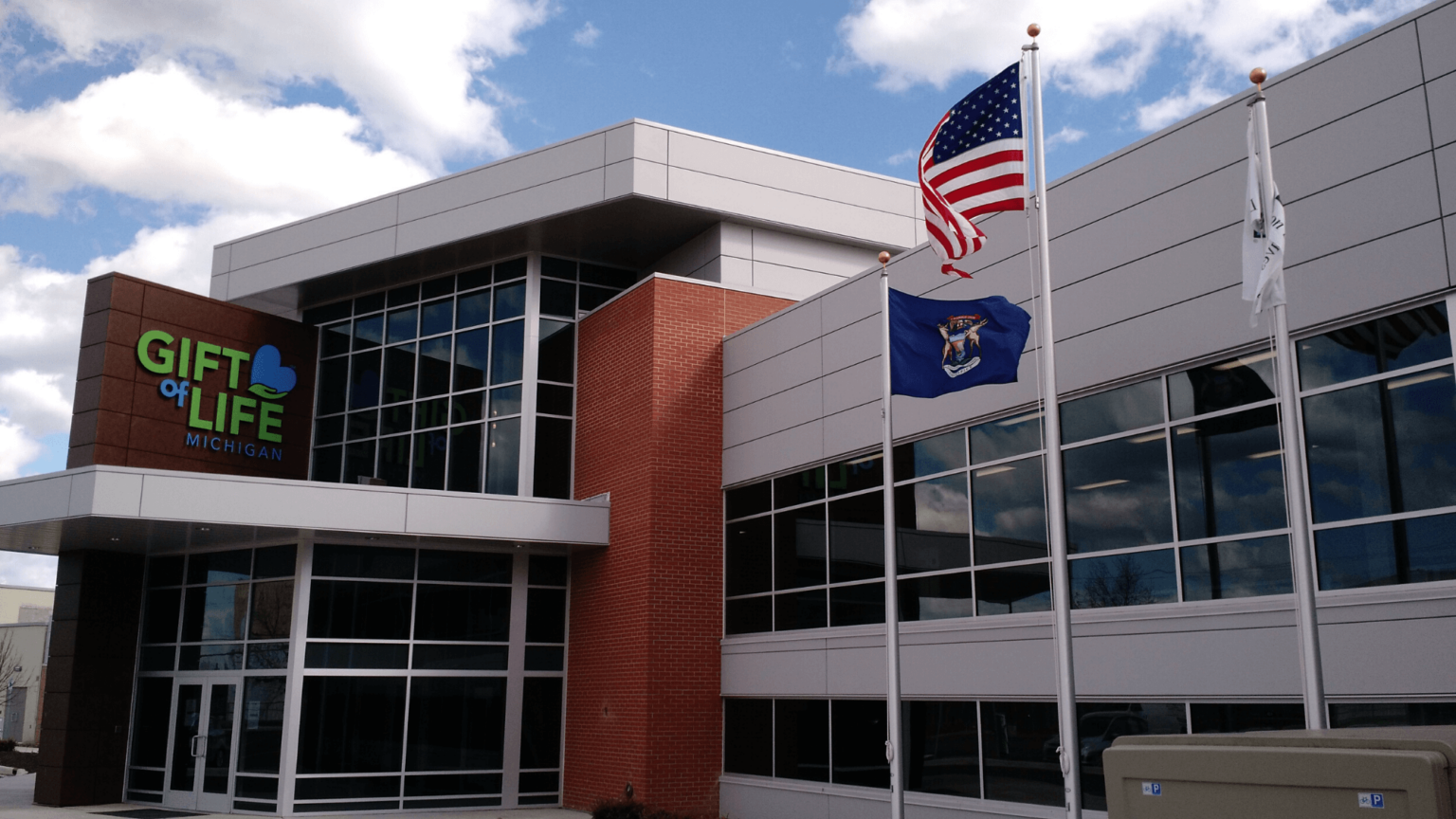 Two-story office building with lots of windows, an American flag and Donate Life flag in front, and the Gift of Life Michigan logo above the entry