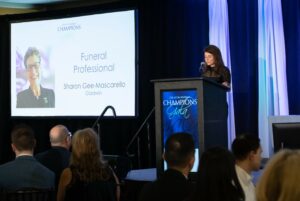 Woman at podium at Gift of Life Champions event, slideshow behind her showing Funeral Professional Champion award recipient