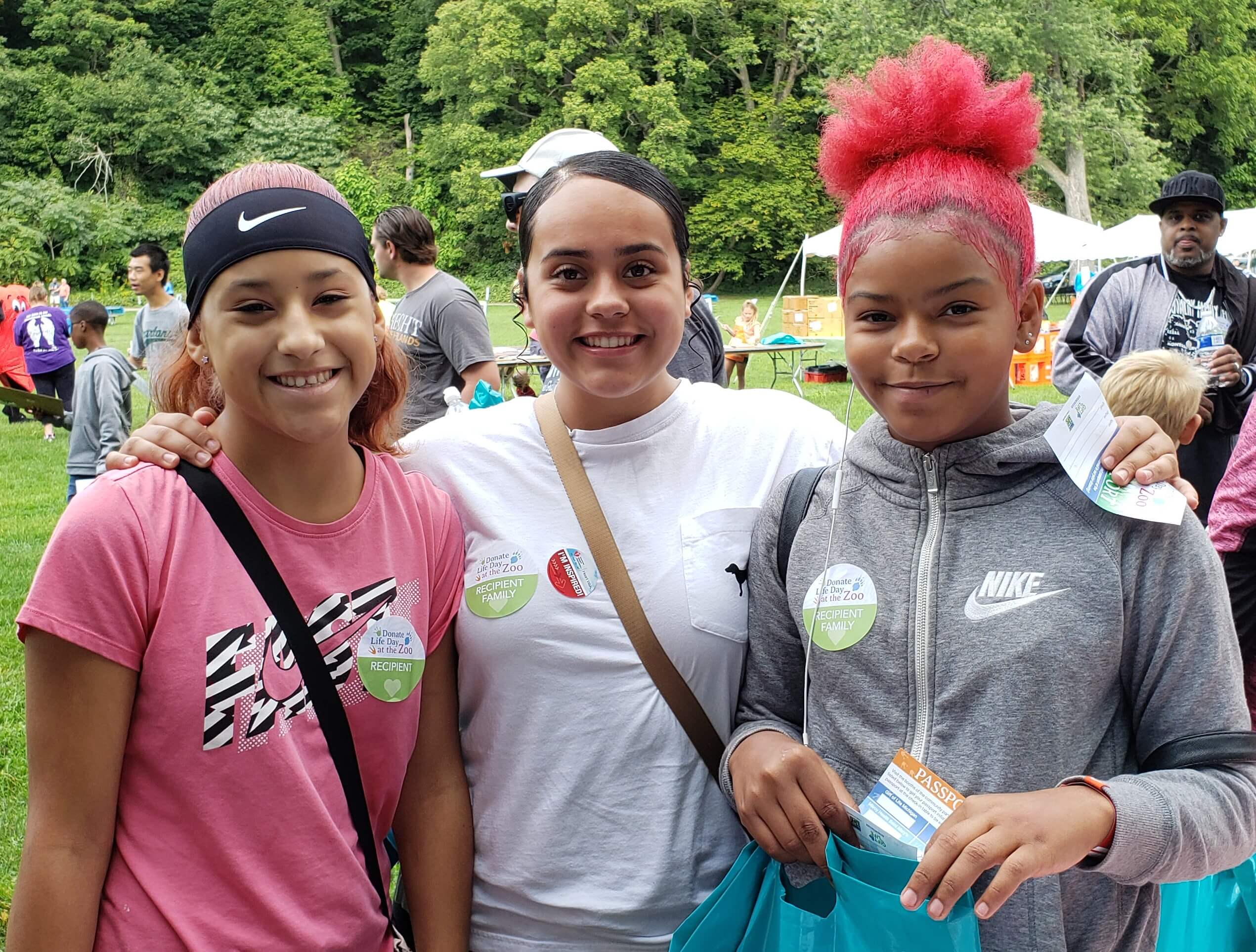 Three young teen girls wearing stickers that identify one as a transplant recipient and the others as family members