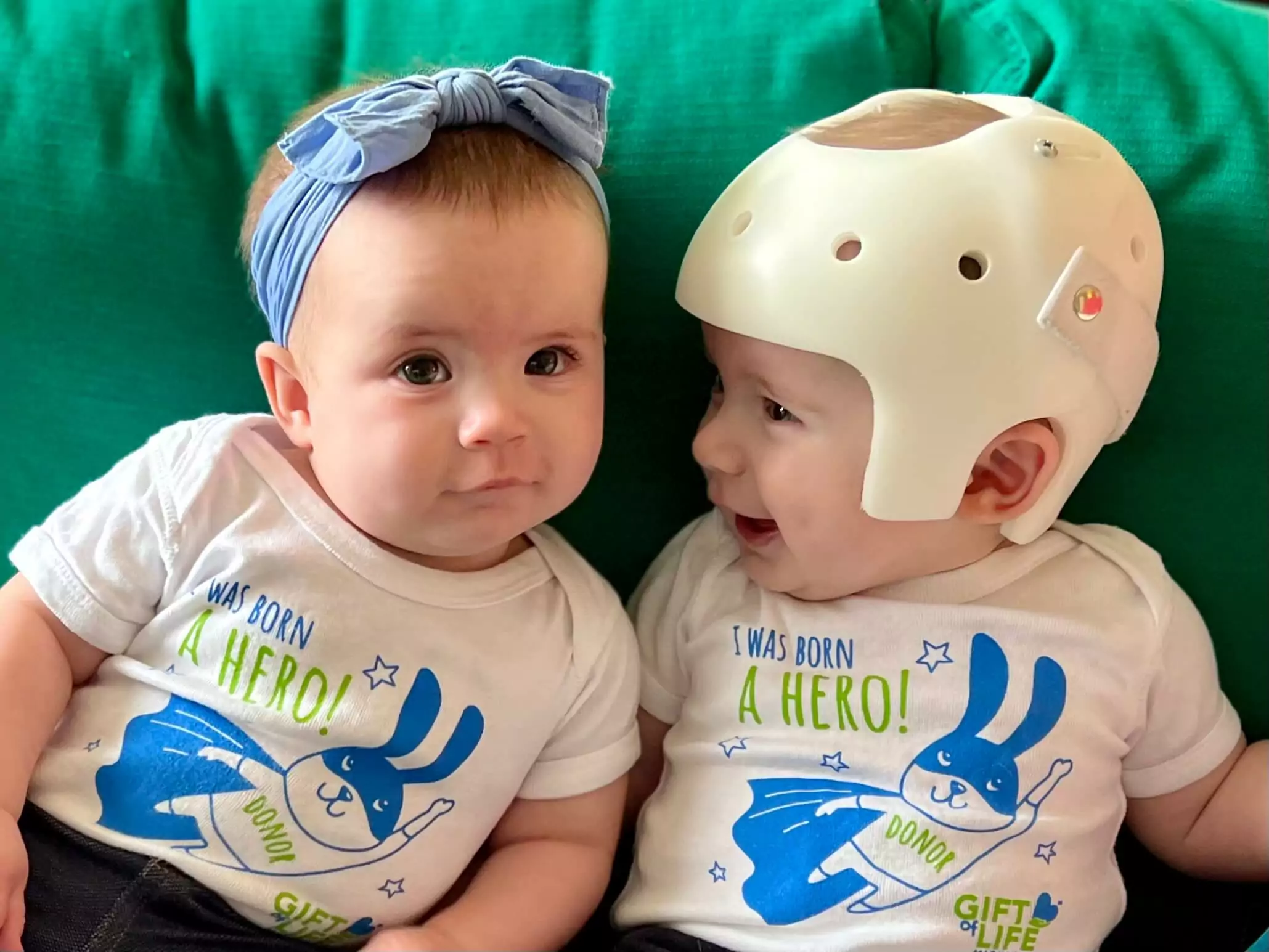 Twin babies wearing shirts with a cute superhero rabbit graphic saying "I was born a hero"