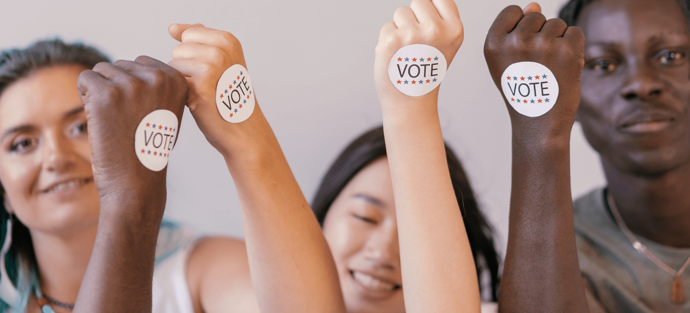 Three people with arms raised, VOTE stickers on the outside of their hands