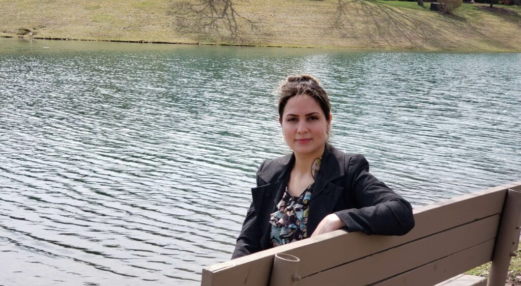 A woman sitting outside on a bench in front of a pond.