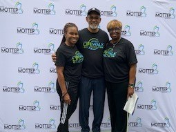 A man and two women in front of a step-and-repeat banner wearing identical t-shirts