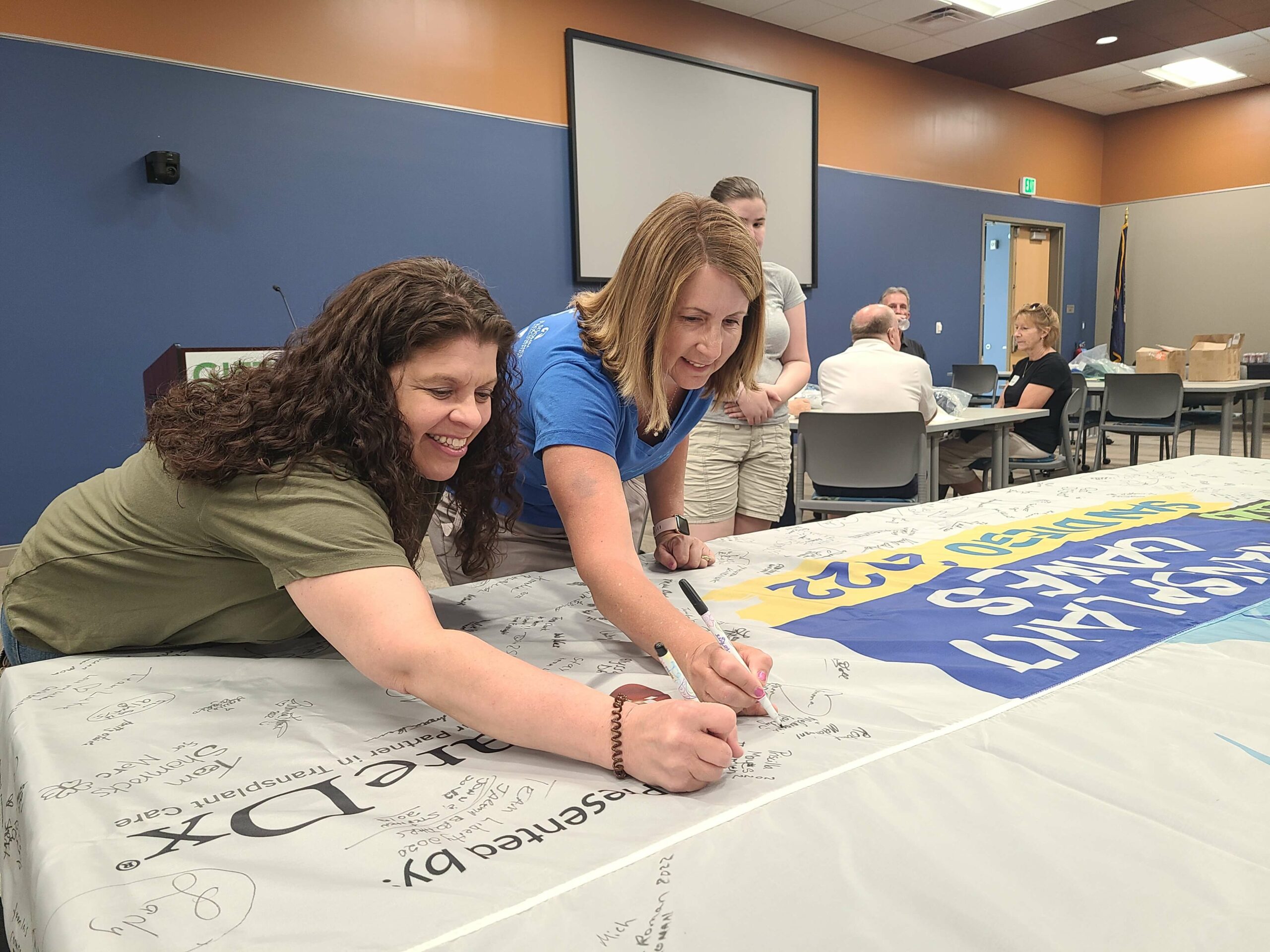 Two women from Team Michigan sign their names to the Transplant Games of America flag