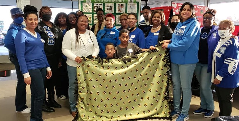 A group of Zeta sisters in blue holding up a comfort blanket they made