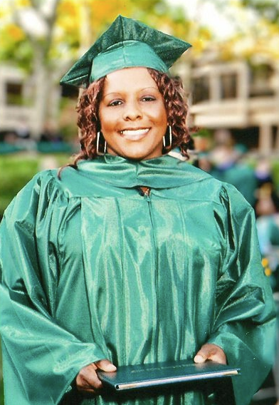 Woman in green robe and graduation cap holding her diploma