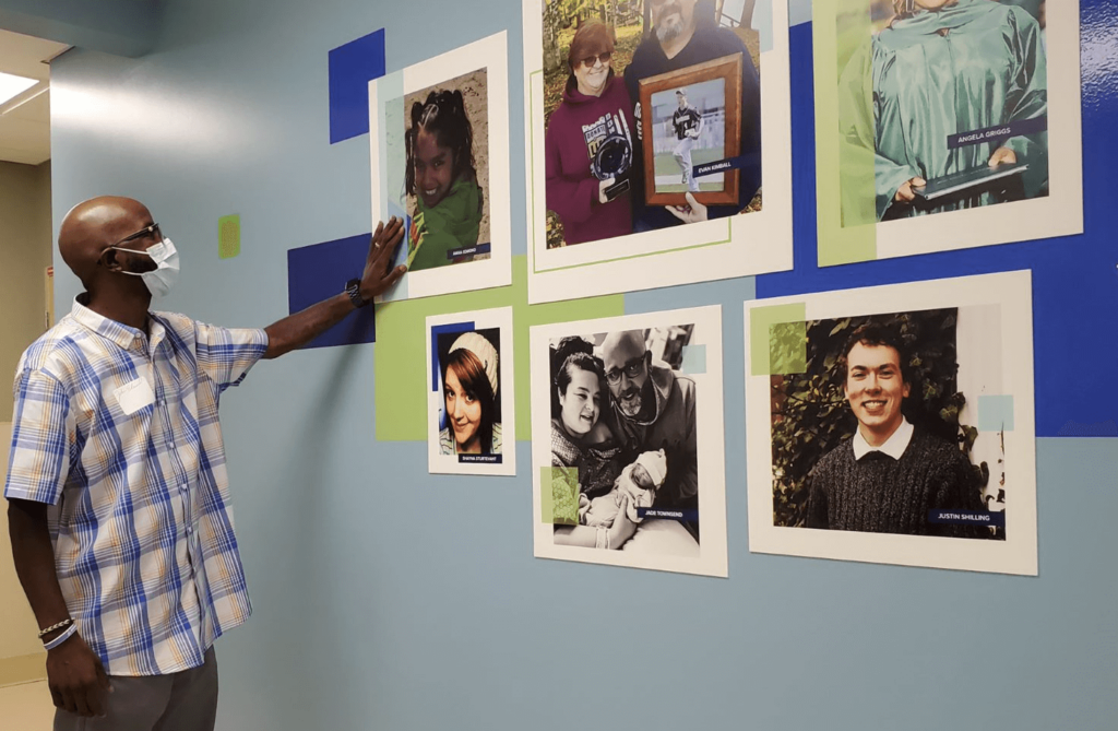 A man reaches his hand out to touch the photo of his daughter on the donation process wall mural at Gift of Life Michigan