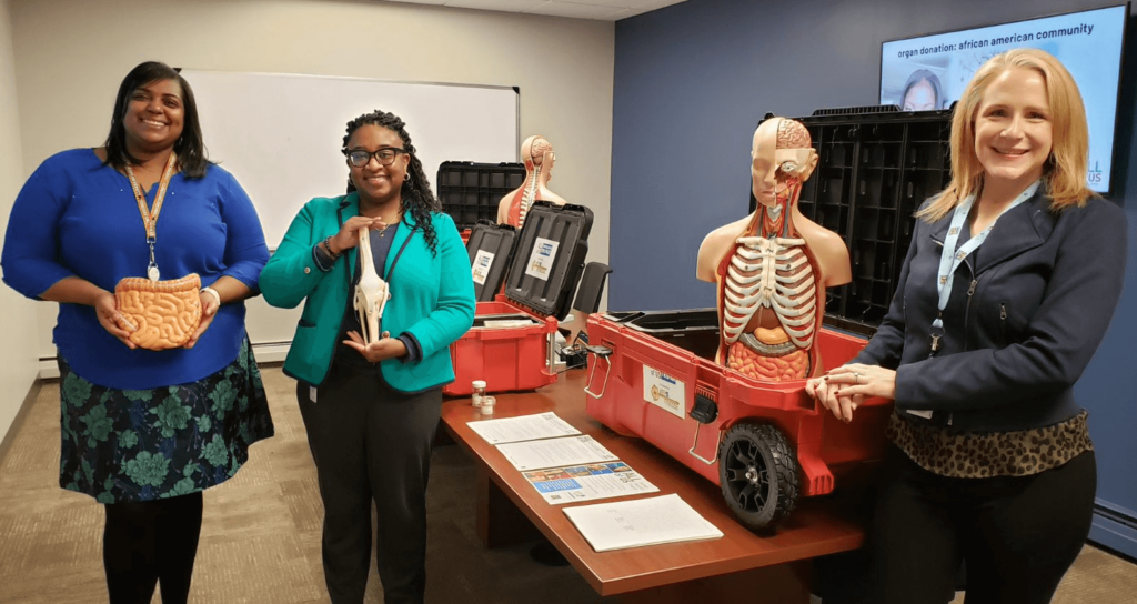 Three women showing an anatomical display with plastic organs and handout materials