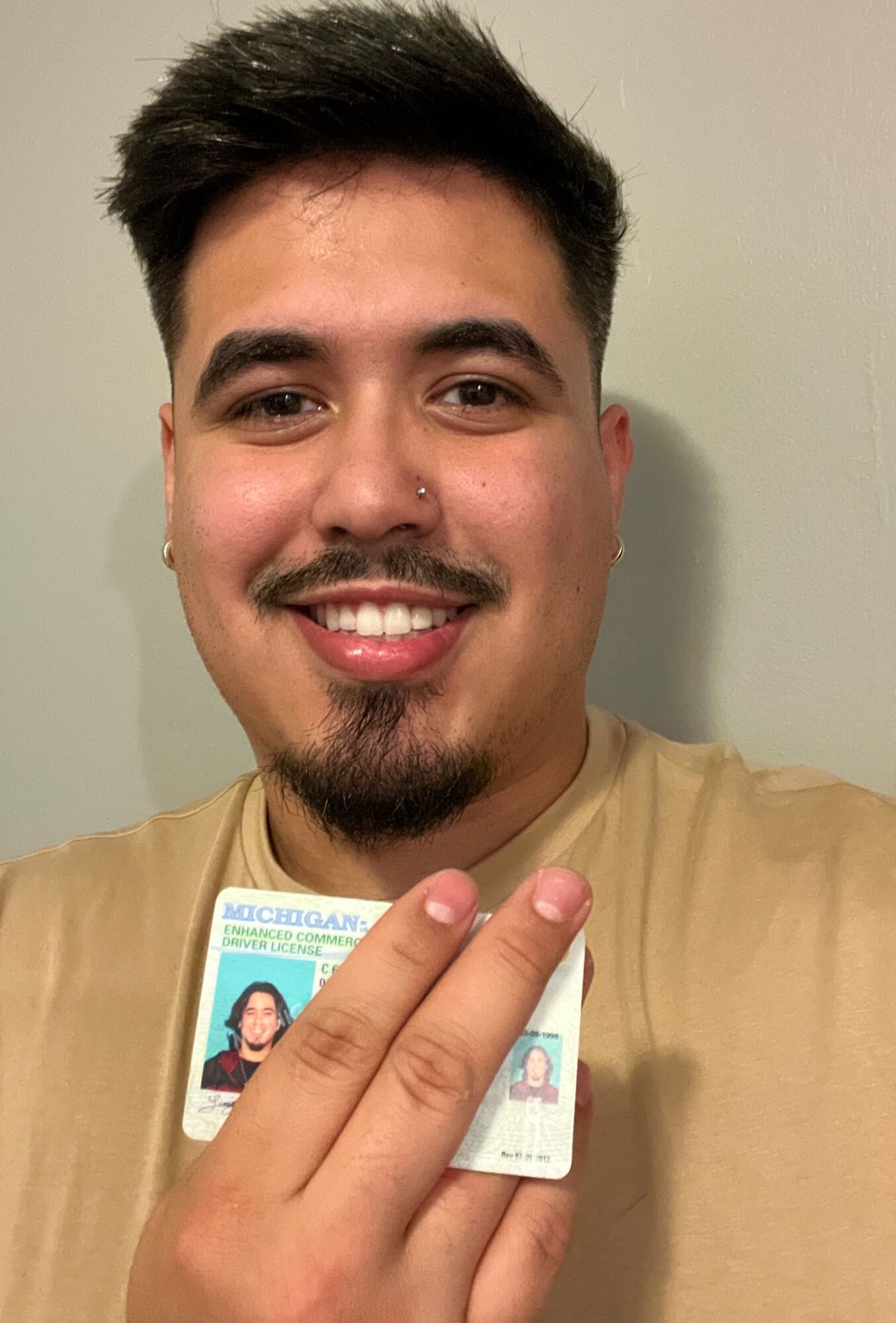 Young Latino man holding up driver's license, no donor heart symbol showing