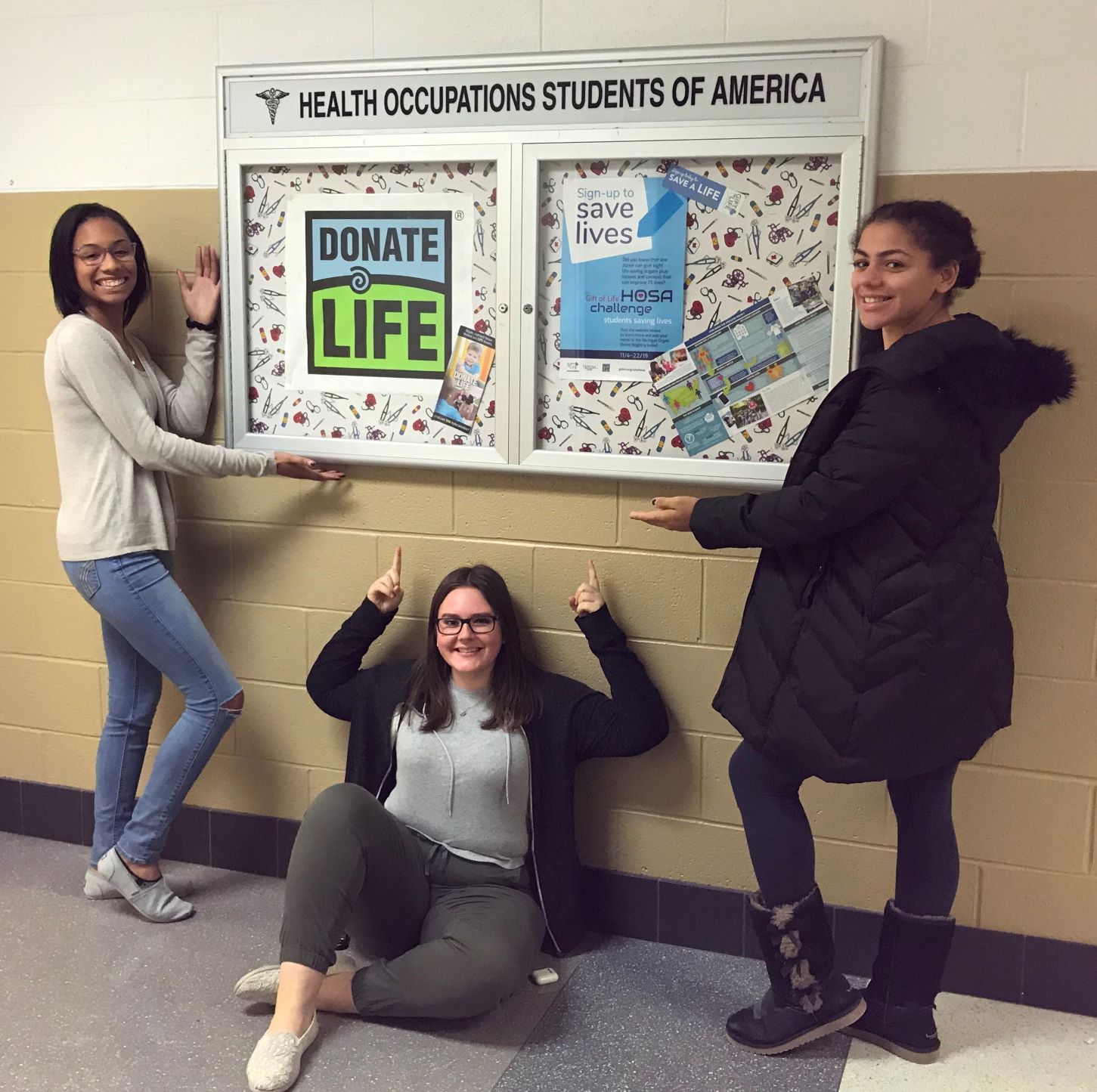 Three HOSA high school students pointing to a display case where they have created a Donate Life/Gift of Life display