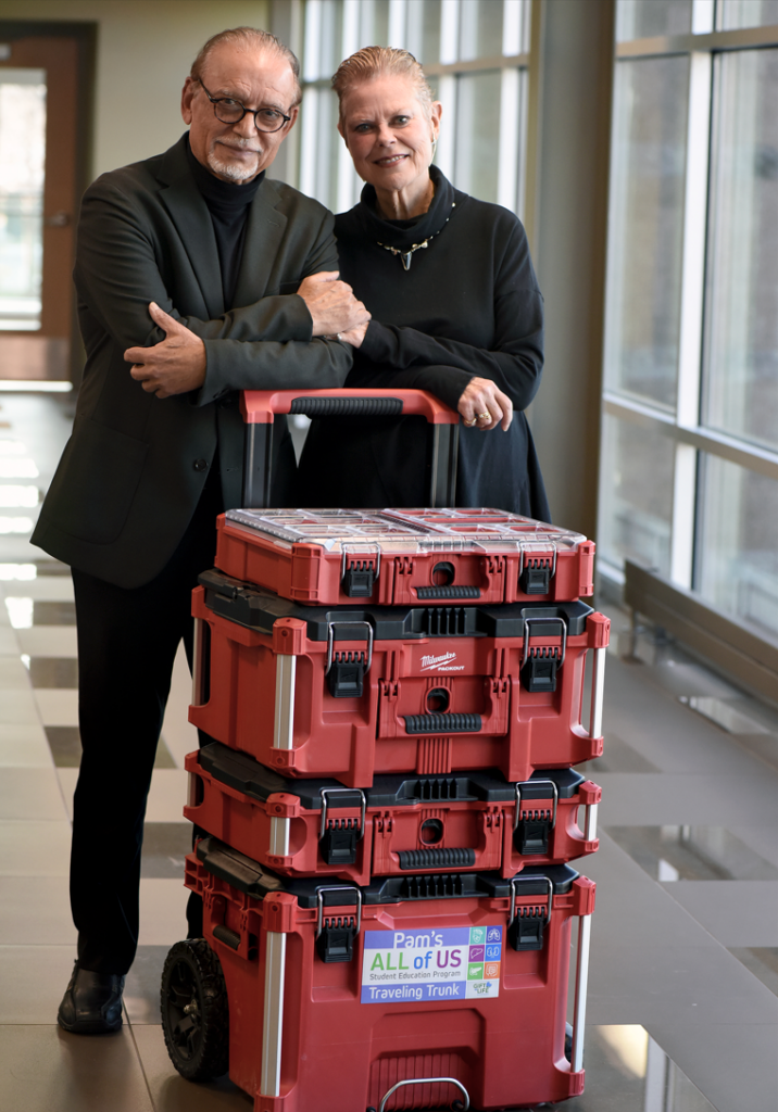 Krishna and Pam Sawhney standing behind a large red traveling trunk on a handcart.