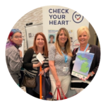 Four women standing in front of a Check Your Heart banner