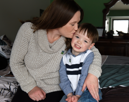 Alyssa Voss plants a kiss on the side of her toddler son Coleton's head as they sit on a bed at home.