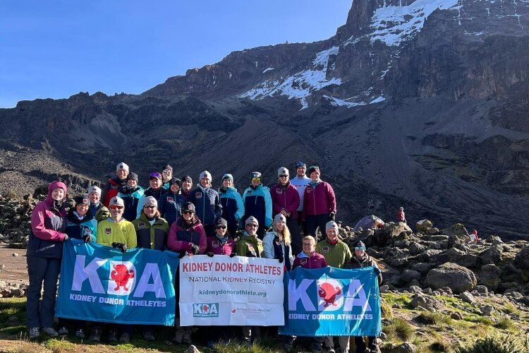 Group of about 20 hikers at a base camp for Mt. Kilimanjaro holding banners in front of them.