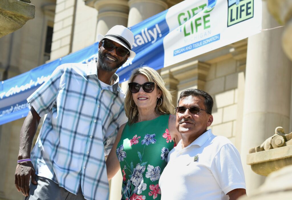 Donor father John Edmond and the recipient of his daughter's liver, Mike Lopez, stand on either side of a Lansing newscaster.