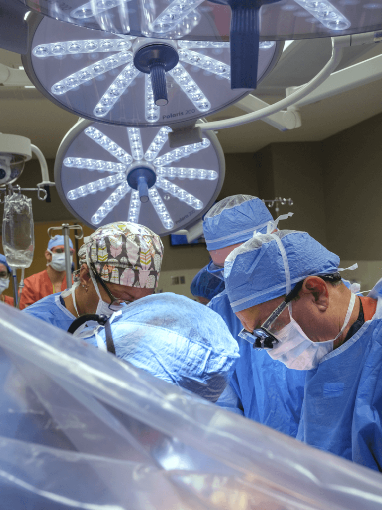 A busy operating room with several masked and gowned people over the operating table.