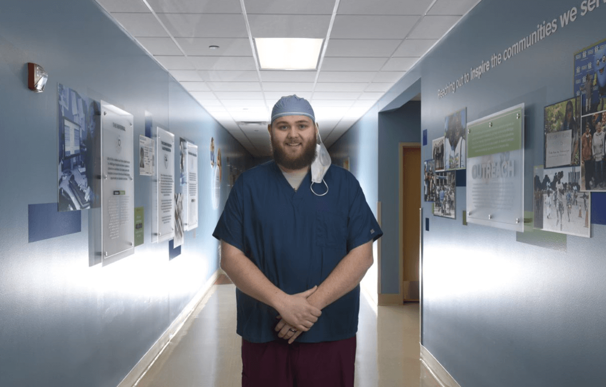 Nick Olden, in scrubs, stands in the Gift of Life Michigan 'Grand Hallway' featuring a mural about the donation process.