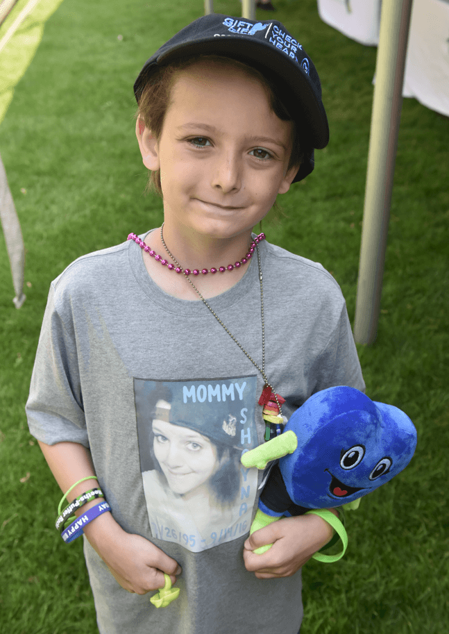 An 8-year old boy holds a stuffed blue heart-shaped Hartley mascot, and wears a shirt with a photo of his mother, Shayna Sturtevant, who was an organ, eye and tissue donor.