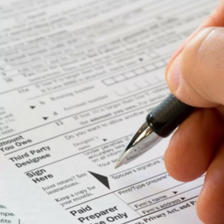 Someone holding a pen signing their state income tax form