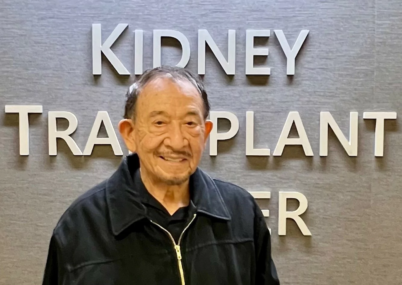 Guadalupe Alejos, who received a kidney transplant 50 years ago, standing in front of the Kidney Transplant Center sign