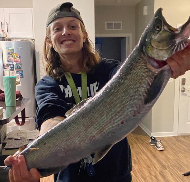 Young man in the kitchen holding up a giant, silver fish