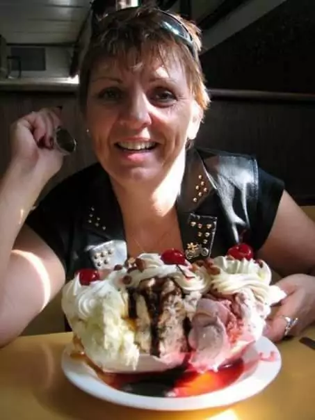 Smiling woman at a restaurant table with a spoon and a giant banana split