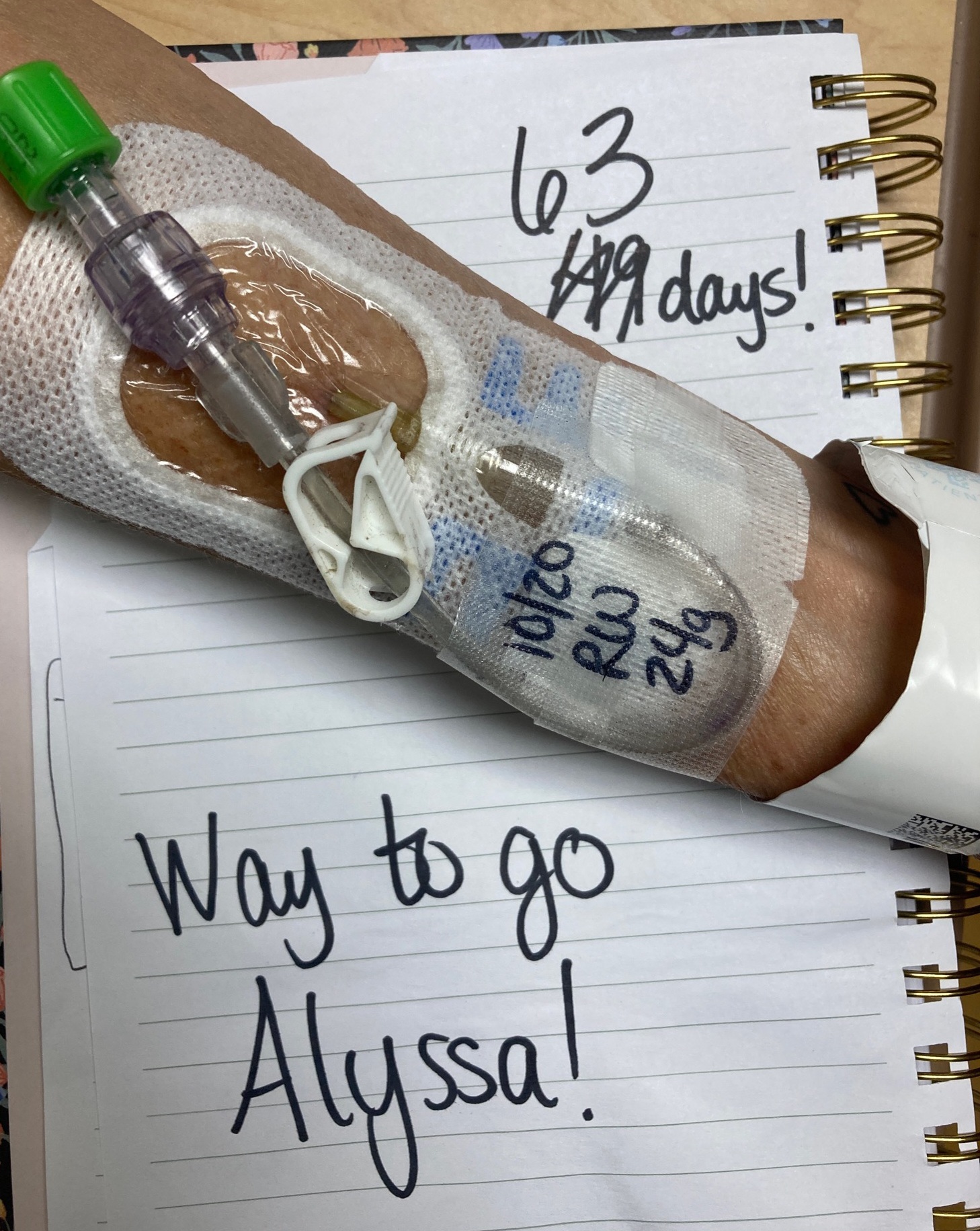 An arm with an IV and a notebook page that reads "63 Days! Way to go Alyssa!"