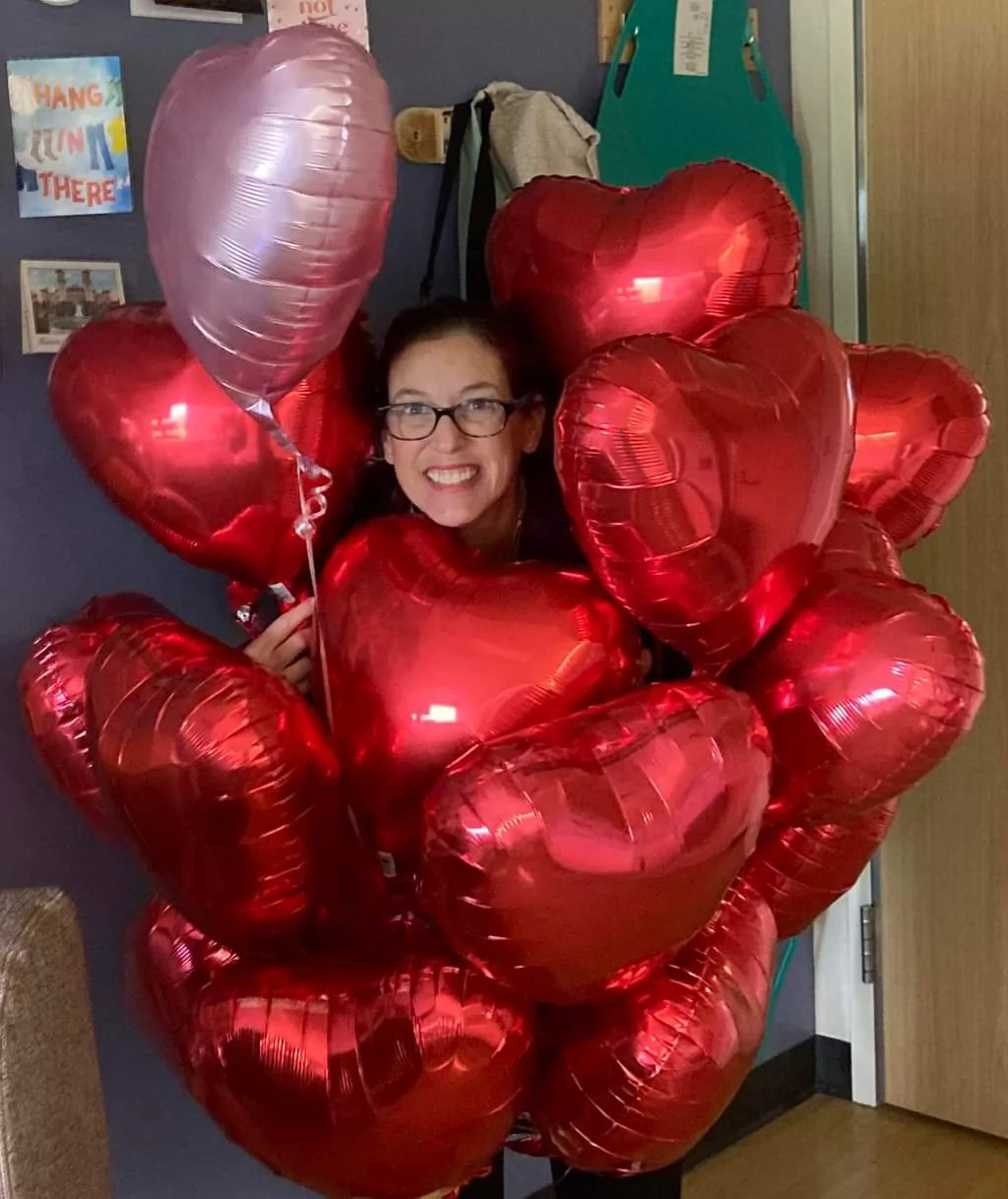 Sherry Johnson holding 17 red heart-shaped balloons