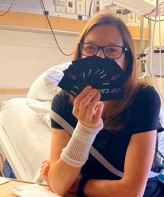 Sherry holding up a handful of Crocs VIP coupons, while sitting on her hospital bed