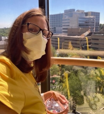 Sherry, in a surgical mask, looking out her window at Michigan Medicine on a bright, sunny day