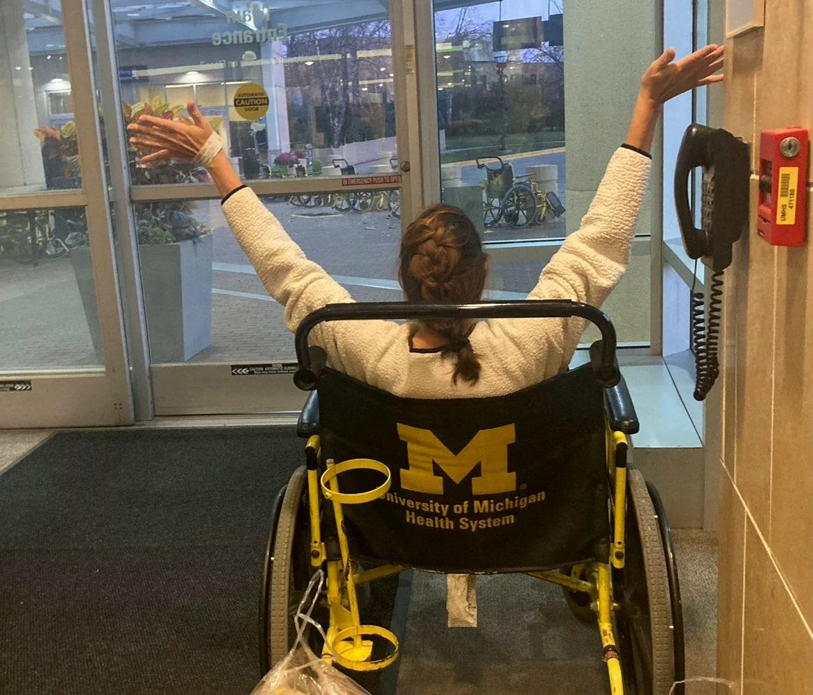 Sherry Johnson is wheelchaired out the front doors of Michigan Medicine with her arms raised up in triumph and excitement after her heart and kidney transplant.
