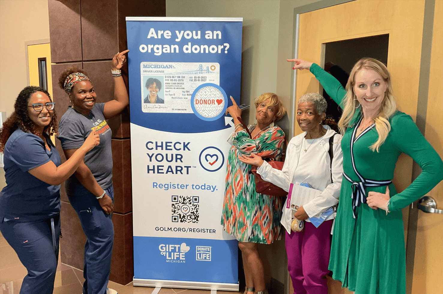 Five women pointing to a vertical banner that asks "Are you an organ donor?" with a driver's license image below that.