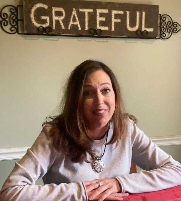 Sherry Johnson, who recently received a heart and kidney transplant, sits below a sign saying "GRATEFUL" in her dining room.