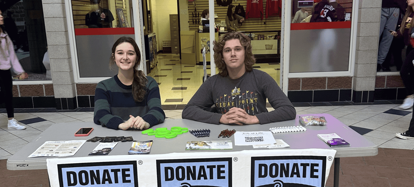 Two high school students at Anchor Bay High School sitting at an information table with Donate Life logos hanging off the front during the HOSA Challenge