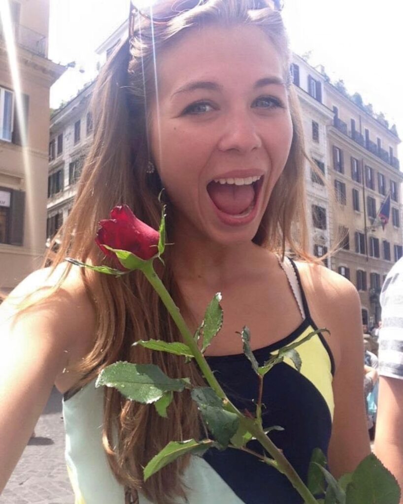 Hailey Brouillet had a fantastic time in Europe shortly before she passed and became an organ donor. Pictured here holding a red rose in front of a tall building.