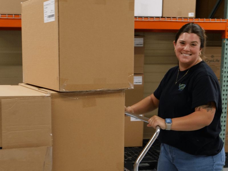 Mackenzie rolling a cart of boxes through the warehouse