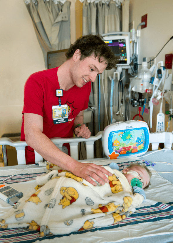 Tommy with infant at Mott His time as a nurse assistant at Mott helping pediatric heart patients is a full-circle experience for Tommy.