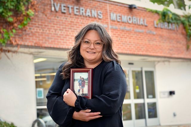 Andrea Graham holds a photo of herself with her brother, standing in front of the Chippewa River District Library