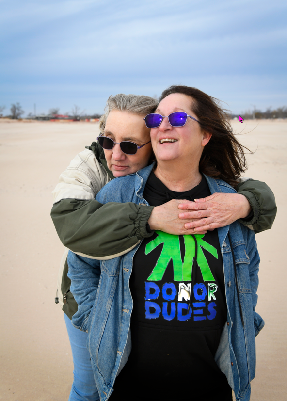 Amanda hugs Becky from behind while standing on a windy beach